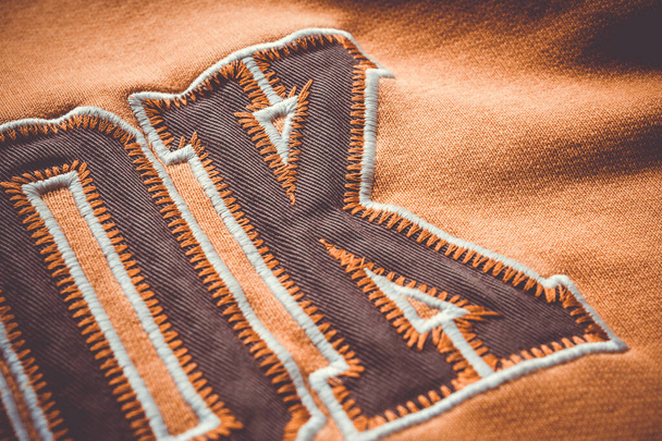 Κοντινό πλάνο στο ύφασμα μιας πορτοκαλί μπλούζας με μερικά γράμματα πριόνι σε αυτό - Φωτογραφία, εικόνα