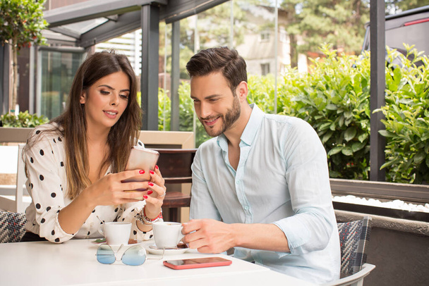 Attractive young couple drinking coffee and watching smart phone in garden restaurant - Fotó, kép