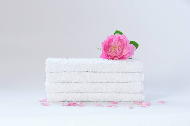 Four white neatly folded terry towels with a rose flower on a light background - 写真・画像
