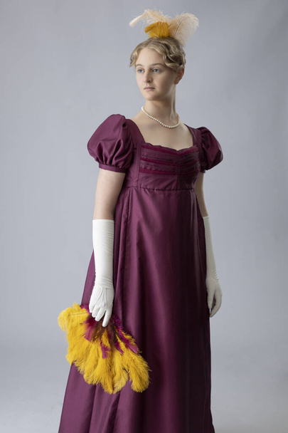 髪に羽のある梅色のイブニングドレスの摂政女性 - 写真・画像