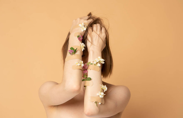 Pretty young girl covering face with hands with flowers and plasters, concept photo for feminist or beauty blog - Fotoğraf, Görsel