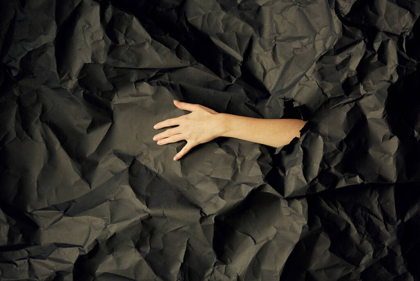 Womans hand comes out of hole in black crumpled paper background, a concept photography for beauty blog - Foto, immagini