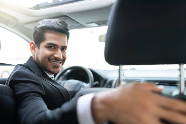 Gülümseyen genç Latin iş adamı arabayla seyahat ediyor. - Fotoğraf, Görsel