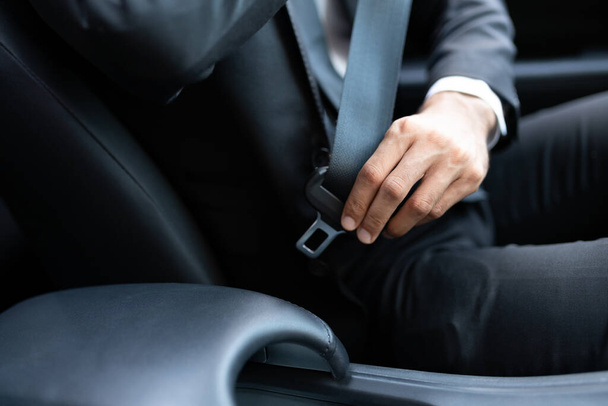 Средняя часть бизнесмена регулирует ремень безопасности во время поездки на автомобиле
 - Фото, изображение