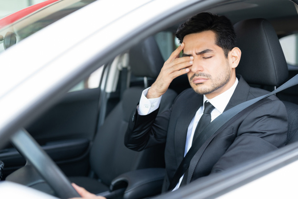 Втомився молодий бізнесмен розтирає очі під час водіння автомобіля
 - Фото, зображення