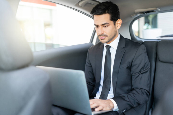 Hispanic young businessman using laptop while traveling in taxi - Foto, imagen