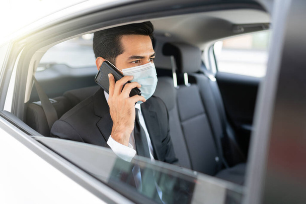 Geschäftsmann telefoniert während der Coronavirus-Krise mit Gesichtsmaske im Taxi - Foto, Bild