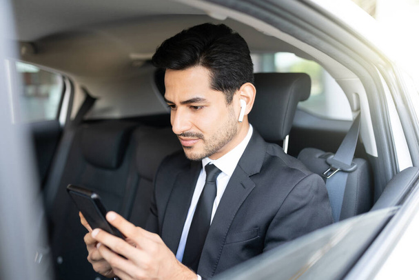 Jóképű latin fiatal üzletember használja okostelefon utazás közben autóval - Fotó, kép