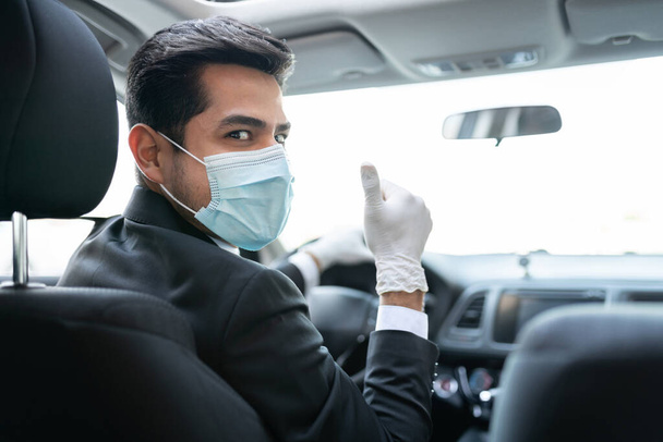 Junger Autofahrer mit Handschuhen und Maske zeigt bei Coronavirus-Krise im Auto Daumen hoch - Foto, Bild