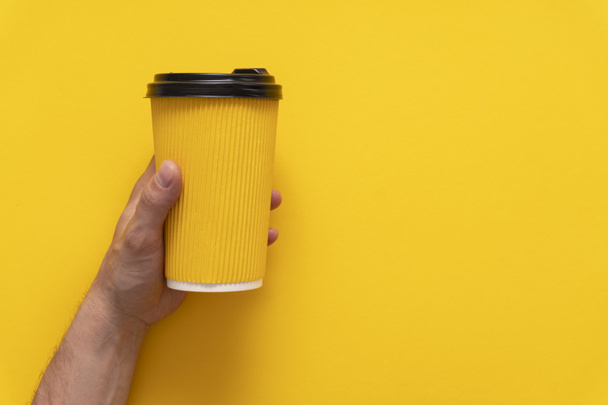 Coffee to go in yellow paper cup in left caucasian hand on yellow background, - Zdjęcie, obraz