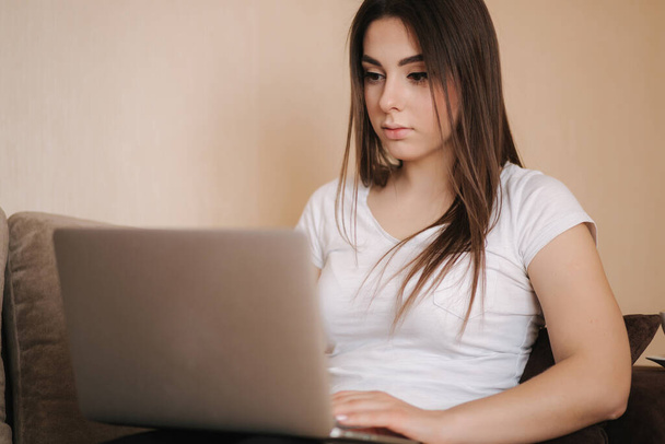 Egy fiatal nő otthon dolgozik a karanténban. A nő laptopot használ a kanapén. Női tanulás távoktatás - Fotó, kép