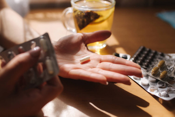 Großaufnahme von Frauenhänden mit Tabletten. Hand mit Tabletten und schwarzem Tee mit Zitrone. Immunität. Vitamine - Foto, Bild