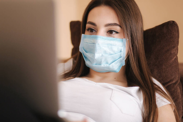 Woman in protective mask working from home during Coronavirus. Woman show that she is healthy and all is OK. Female self isolated at home in room - Photo, image