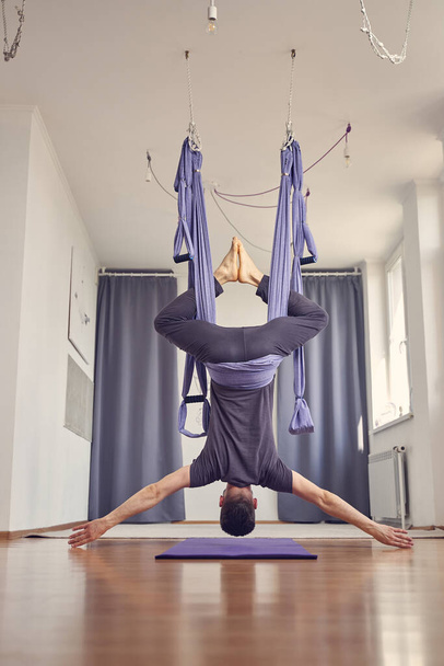Athletic young man hanging upside down in yoga studio - Фото, зображення