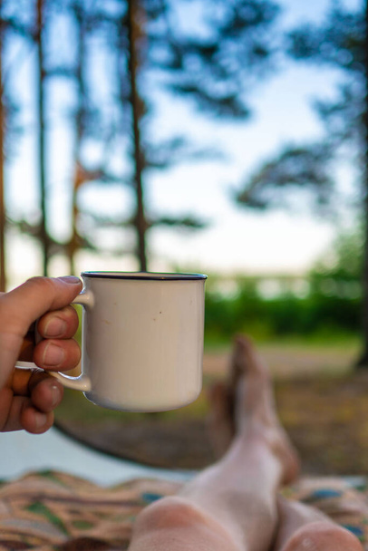 camping in the forest. White camping cup with tea on a forest background. summer camping - Foto, Imagem