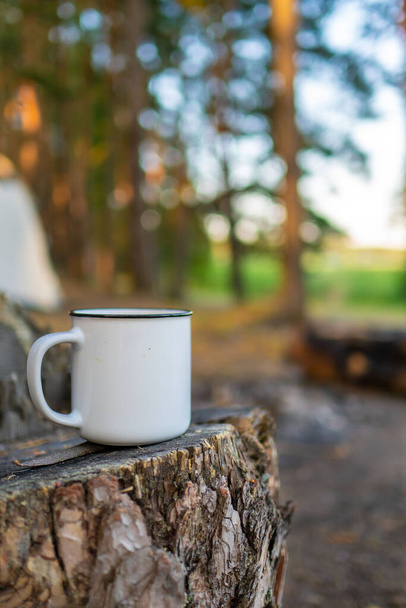 camping in the forest. White camping cup with tea on a forest background. summer camping - Fotó, kép