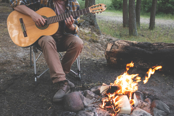 camping in the woods. man plays the guitar by the fire in nature. summer camping. relaxation in nature - Photo, image