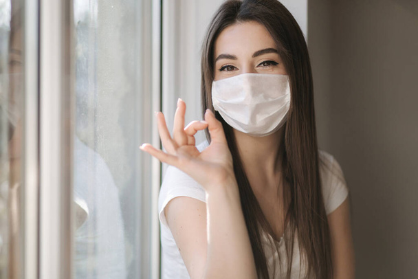 Young woman take off protective mask. Female in white t-shirt and white medical mask. End of quarantine. Coronavirus theme - Photo, image