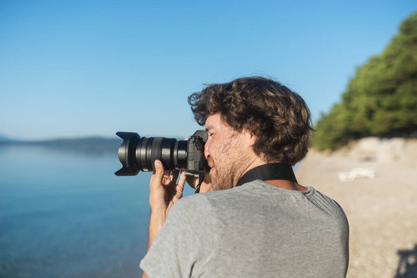 若い男性写真家は彼のプロのdslrカメラで早朝に美しい海と自然の写真を撮る. - 写真・画像
