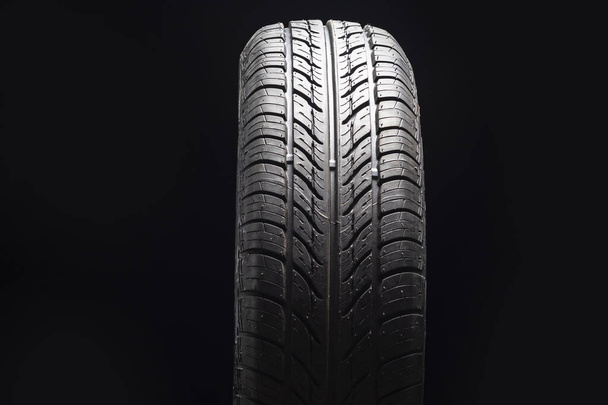 Car tire in dark color. Night shooting. The tread is summer. Light falls from above. - Photo, Image