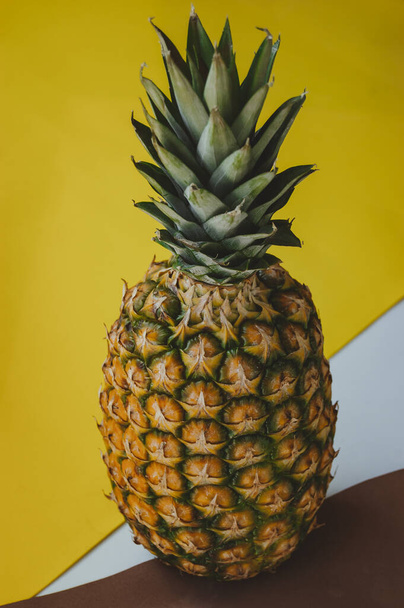 ripe juicy tropical pineapple on a yellow-white background. Space for text. Pineapple on a wooden table - Фото, изображение