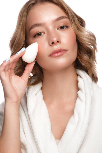 Beautiful tender young girl in a white coat with clean fresh skin posing in front of the camera with a sponge in her hands. Beauty face. Skin care. - Foto, imagen