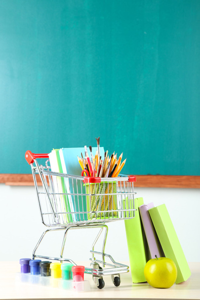 School supplies in supermarket cart on blackboard background - Valokuva, kuva