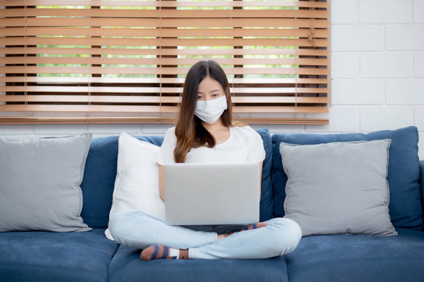 Young asian business woman in face mask work from home on laptop computer online to internet in living room, girl in medical mask and quarantine for pandemic of covid-19, stay home, new normal. - Φωτογραφία, εικόνα