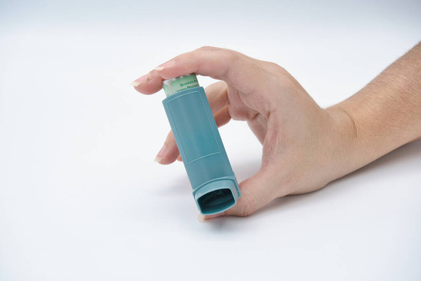 Το χέρι μιας γυναίκας που κρατάει έναν εισπνευστήρα άσθματος σε λευκό φόντο - Φωτογραφία, εικόνα