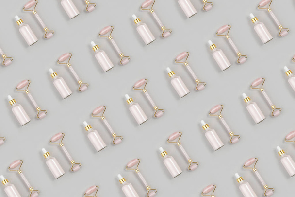 Cosmetic pattern. Crystal rose quartz facial roller and anti-aging collagen, serum in glass bottle on grey background. Facial massage for natural lifting, Beauty concept Top view Flat lay. - 写真・画像