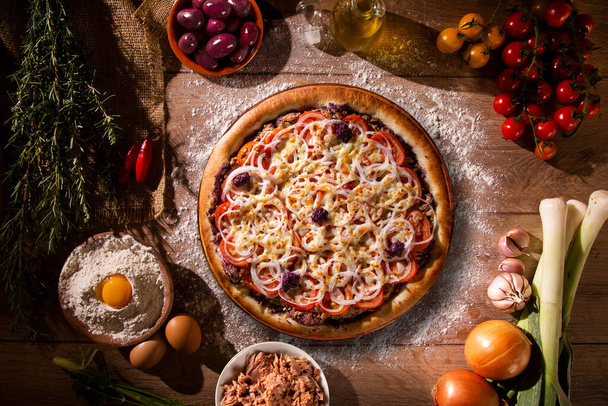Pizza tuna fish, onion, tomato and black olive on wood background. Top view, close up. Traditional Brazilian Pizza - Fotó, kép