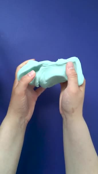 Playing with slime, stretching the gooey substance for fun and stress relief. Close up and top view of female hand holding blue shining slime, squeezing it. - Video, Çekim
