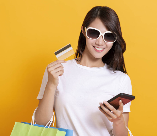 χαρούμενη νεαρή γυναίκα με καλοκαιρινό φόρεμα και χρήση κινητού τηλεφώνου online αγορές με πιστωτική κάρτα - Φωτογραφία, εικόνα