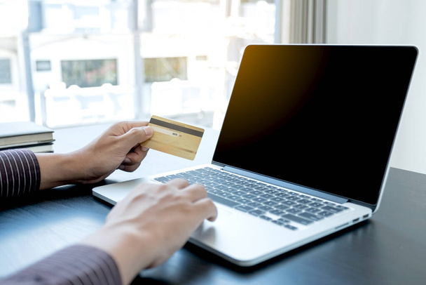 La mano del hombre de negocios sostiene una tarjeta de crédito y utiliza un ordenador portátil para compras en línea y pago por Internet en la oficina. - Foto, Imagen