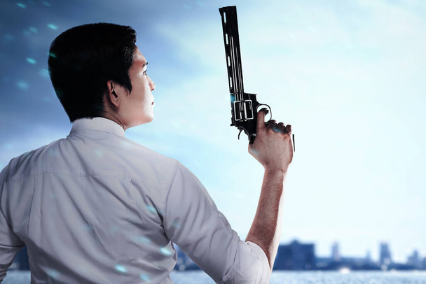 Asian man standing with a gun on his hand on the city with the night scene background - Foto, Imagen