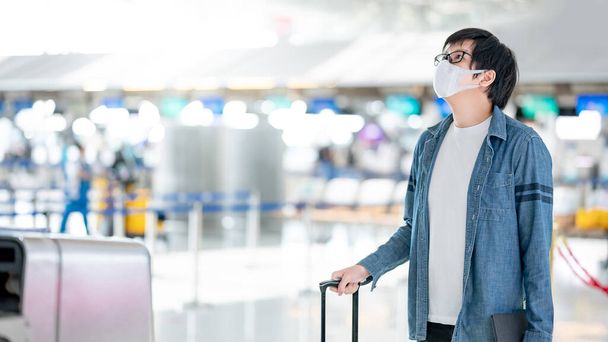 Ázsiai férfi turista maszkot visel bőrönddel a check-in pultnál a repülőtér terminálján. Coronavirus (COVID-19) világjárvány megelőzése utazás közben. Egészségügyi tudatosság és társadalmi távolság - Fotó, kép