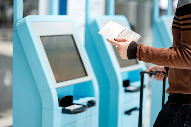 Мужчина, имеющий паспорт и смартфон с помощью киоска саморегистрации в терминале аэропорта. Концепция поездки за границу - Фото, изображение