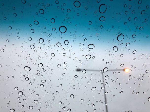 gouttes de pluie sur le toit ouvrant de la voiture avec poteau de lampe sur la toile de fond de la rue - Photo, image