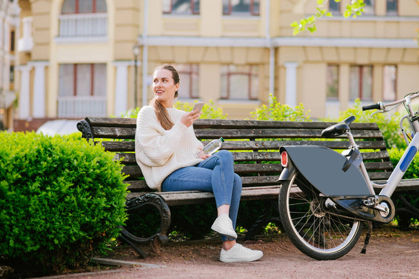 Young woman sitting in park on bench near bicycle - Foto, Imagem