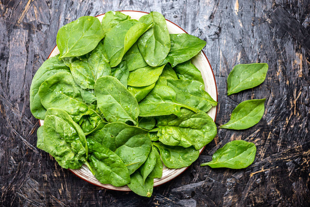 Grüne Blätter von frischem Spinat in einem Teller auf dunklem Hintergrund. Gesunde vegetarische Kost. Der Blick von oben. - Foto, Bild