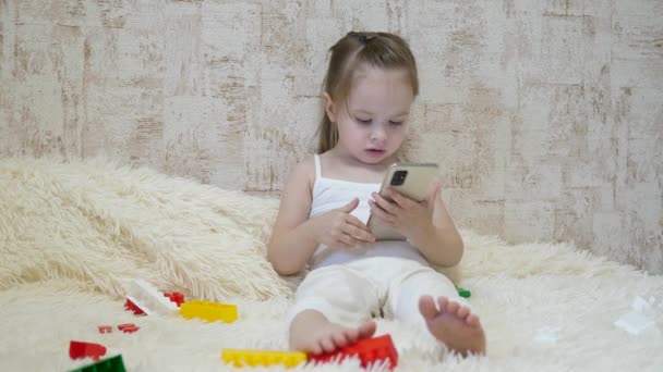 El niño juega en el teléfono inteligente en la habitación. Aprendizaje a distancia de preescolares en línea - Imágenes, Vídeo