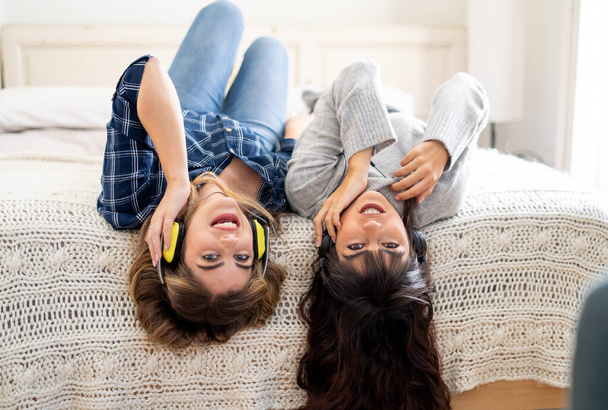 COVID-19 lockdown. Confident and optimistic women best girlfriends laughing listening online music singing and dancing together in bed at home in isolation. Stay home safe health and safety campaign. - 写真・画像