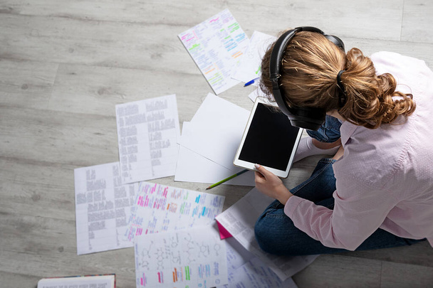 online εκπαιδευτική έννοια. Κορίτσι με ακουστικά κρατά tablet και κοιτάζει τις σημειώσεις. Άνω όψη - Φωτογραφία, εικόνα