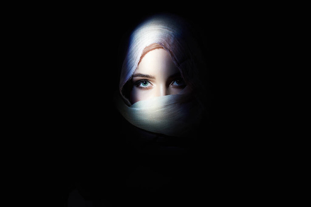 красивая молодая женщина в хиджабе, смотрит из темноты. Красавица в капюшоне. Восточная женщина моды
 - Фото, изображение