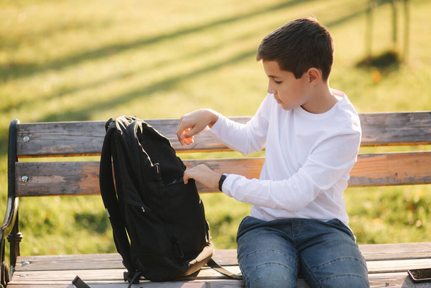 Akıllı telefonu şarj etmek için sırt çantasındaki güç kabuğundan al. Sonbahar zamanı parkta tatlı bir çocuk. - Fotoğraf, Görsel