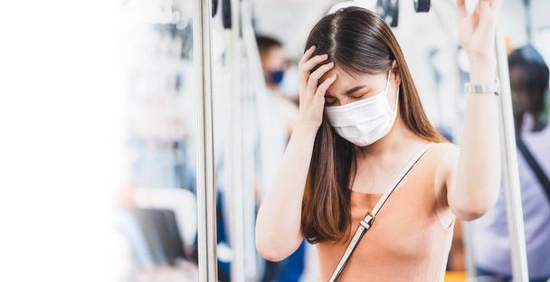 Jeune femme asiatique portant un masque chirurgical et ayant mal à la tête dans un train de métro lors d'un voyage dans une grande ville lors de l'épidémie de Covid19, Infection et pandémie, nouveau concept de prévention normale et de la maladie - Photo, image