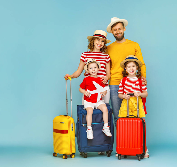 Full body happy family parents and children with luggage smiling and looking at camera against blue backdro - Φωτογραφία, εικόνα