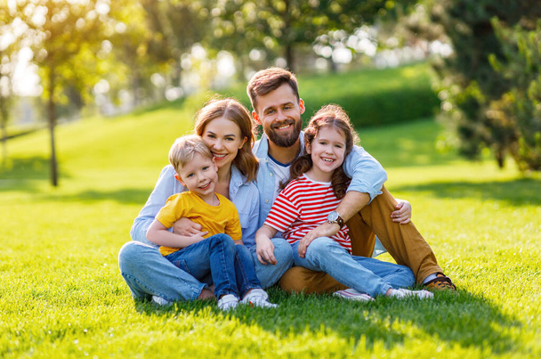 Веселая счастливая семья обнимается и смотрит в камеру, отдыхая на зеленой траве в солнечный день.
 - Фото, изображение