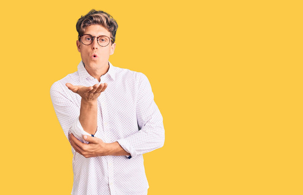 Young handsome man wearing business clothes and glasses looking at the camera blowing a kiss with hand on air being lovely and sexy. love expression.  - Foto, Imagem