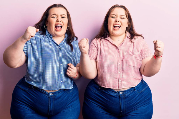 Young plus size twins wearing casual clothes angry and mad raising fists frustrated and furious while shouting with anger. rage and aggressive concept.  - Фото, изображение